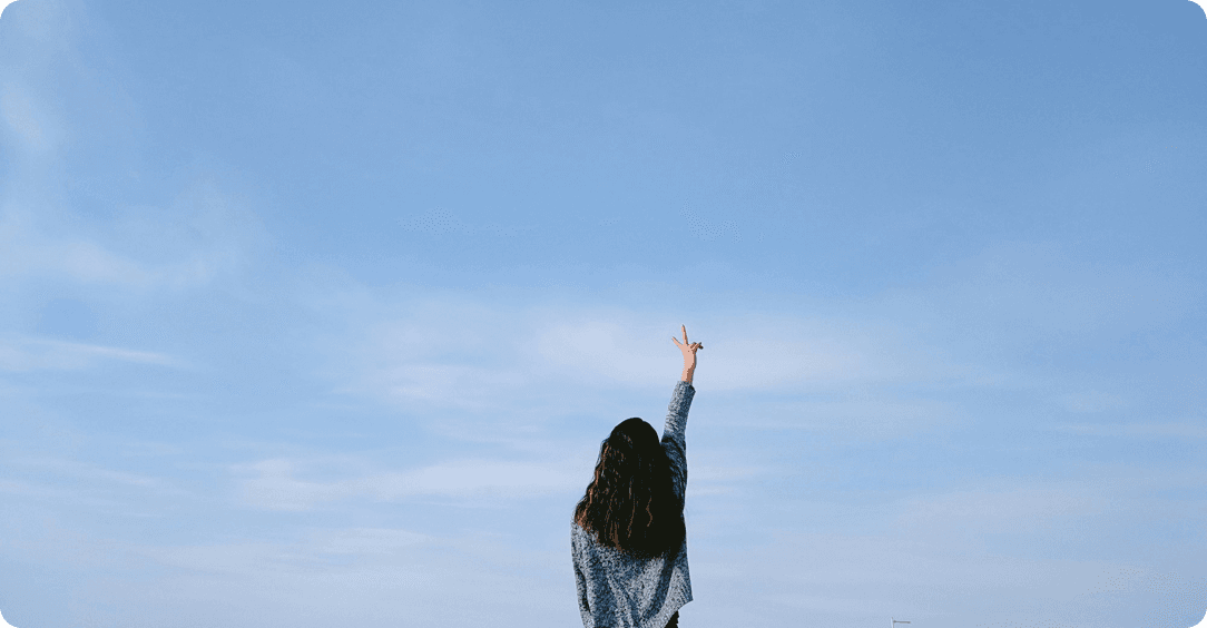 Donna di spalle che fa il segno della vittoria con cielo azzurro di sfondo