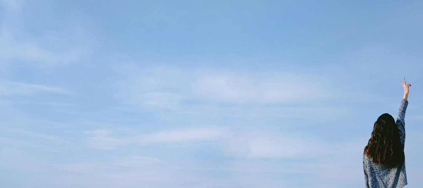 Donna di spalle che fa il segno della vittoria con cielo azzurro di sfondo