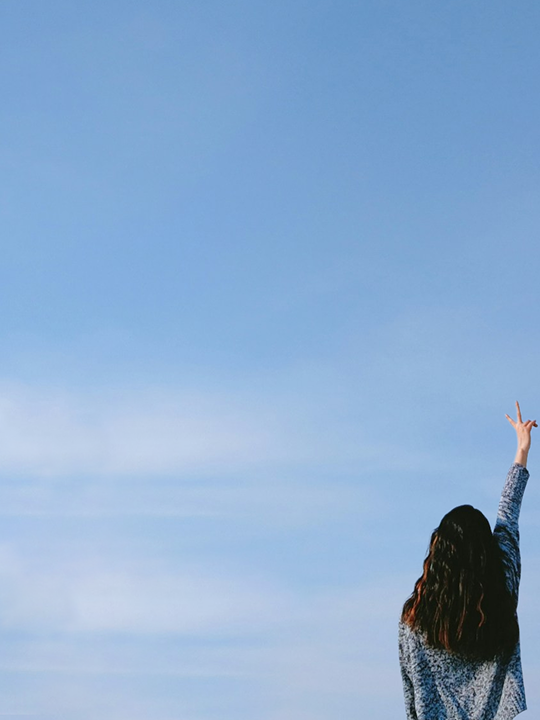 Donna di spalle che fa il segno della vittoria con cielo azzurro di sfondo